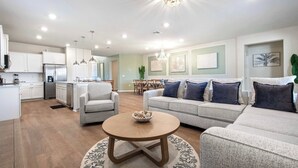 A modern living room with a round coffee table, a grey sofa, and a dining area in the background.