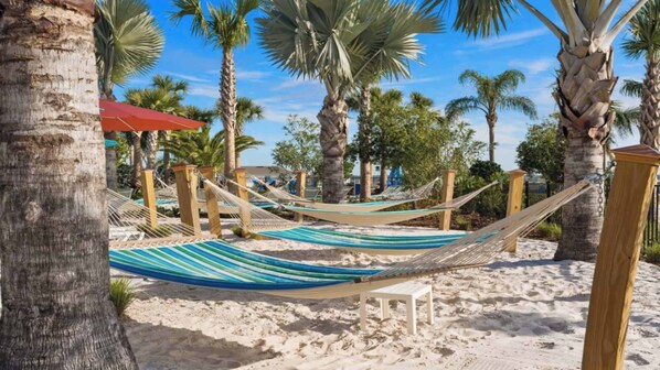 Una playa con hamacas colgadas entre postes de madera, una silla blanca y palmeras.