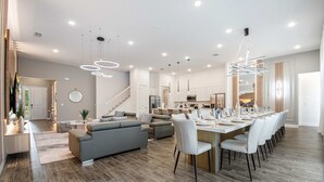 Ein geräumiger Wohnbereich mit einer modernen Küche, einem Essbereich mit großem Tisch und einer Treppe, die zu einer oberen Etage führt.