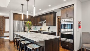 Una cocina moderna con gabinetes de madera oscura, electrodomésticos de acero inoxidable y una isla de mármol con taburetes de bar.