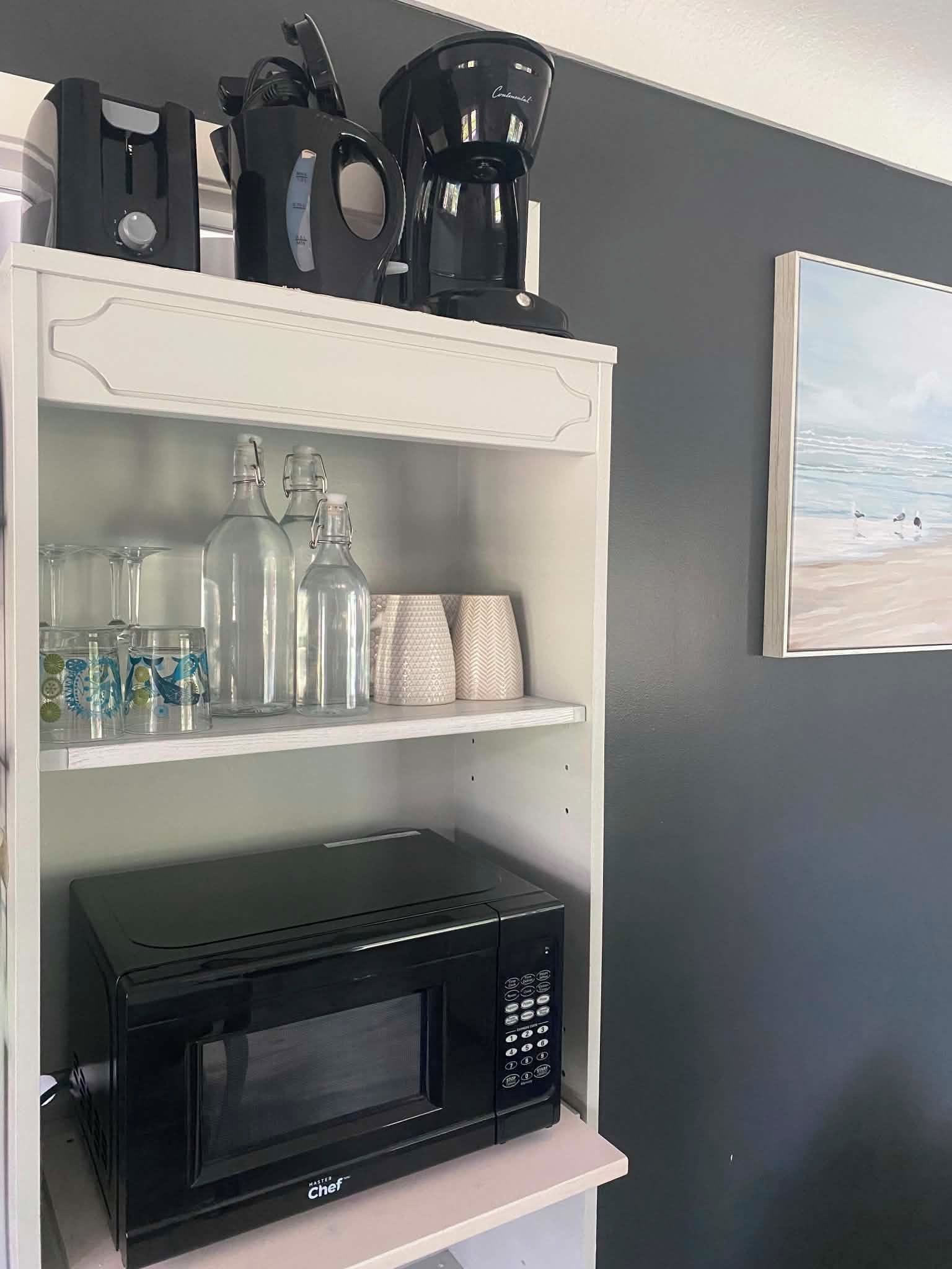 A kitchen area with a microwave on a white shelf, a coffee maker, and various glass containers.