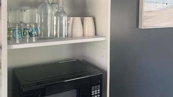 A kitchen area with a microwave on a white shelf, a coffee maker, and various glass containers.