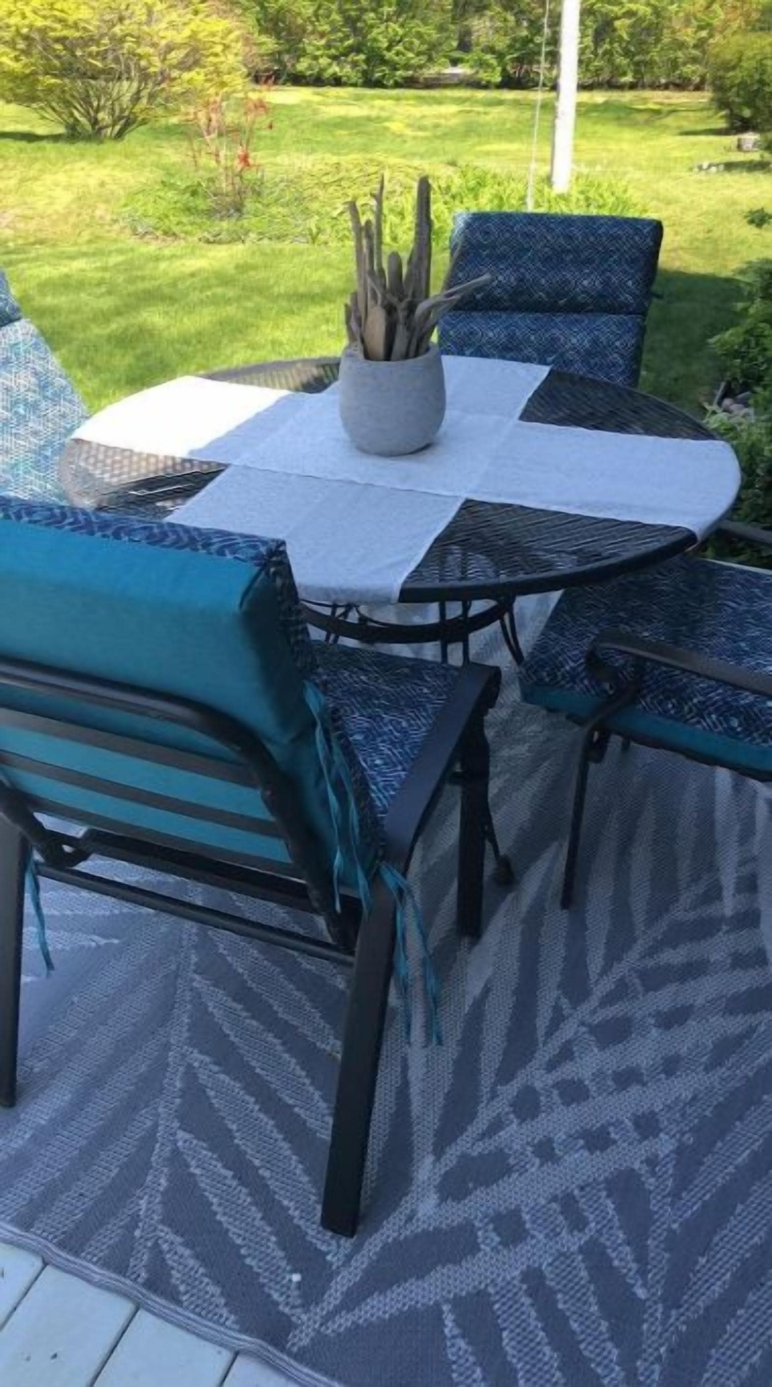 An outdoor patio with a round table and four chairs, a potted plant, and a patterned rug.