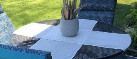 An outdoor patio with a round table and four chairs, a potted plant, and a patterned rug.