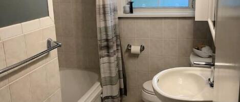 A small bathroom with a shower, toilet, sink, and a window.