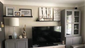 Un salon avec un téléviseur à écran plat posé sur un meuble, une lampe, des objets décoratifs et un meuble avec des portes en verre.