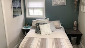 Une chambre à coucher avec un lit, une fenêtre, une table de chevet et des œuvres d’art murales.