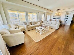 A spacious living room with a large sectional sofa, a coffee table, and a dining area with a chandelier. - Oceans Edge Oceanfront 3BR Villa with Golf Cart (Daufuskie Island)