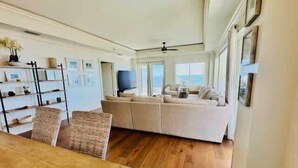A spacious living area with a large sofa, a wooden dining table, and a TV.