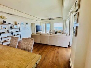 A spacious living area with a large sofa, a wooden dining table, and a TV. - Oceans Edge Oceanfront 3BR Villa with Golf Cart (Daufuskie Island)