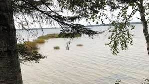 Eine Holztreppe führt zu einem Sandstrand, im Hintergrund ist ein See zu sehen.