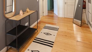 Un couloir doté d’un plancher en bois, d’une console noire avec un miroir, d’un tapis à motifs et d’un grand miroir appuyé contre le mur.
