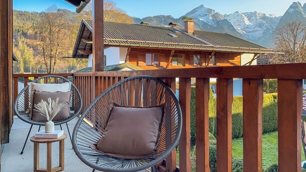 Un balcon avec deux fauteuils en osier, une petite table en bois et une vue sur un paysage montagneux.