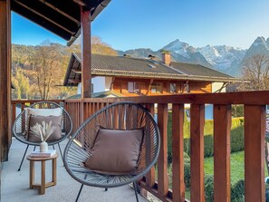 Een balkon met twee rieten stoelen, een tafeltje en uitzicht op een berglandschap.
