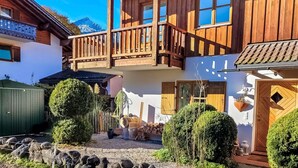 Un chalet traditionnel en bois, doté d’un balcon, entouré d’arbustes soigneusement taillés et bordé d’une allée en gravier.