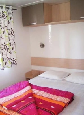 A hotel room with a bed, a nightstand, a wooden headboard, and a wall-mounted cabinet.