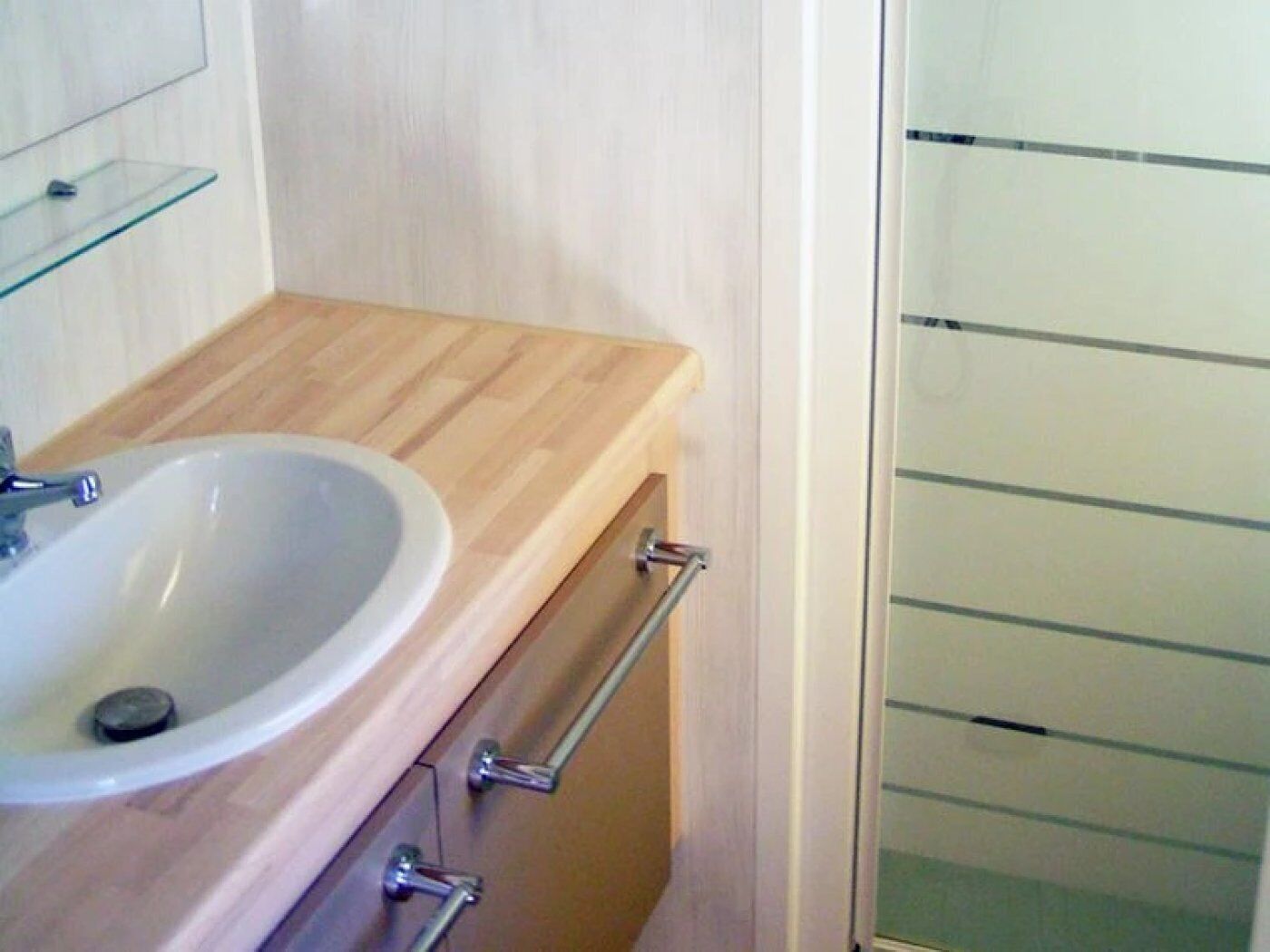 A bathroom with a wooden vanity, a white sink, and a glass shower enclosure.