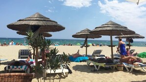 A beach with thatched umbrellas, lounge chairs, and people relaxing.