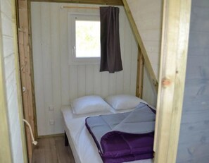 A small, narrow room with a single bed, a window with a curtain, and wooden beams on the ceiling. - ZEcamping 3* animé piscine chauffée locatif TV BBQ clim 36m2 6 pers (Argentonnay)