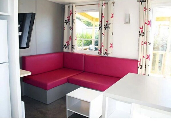 A room with a red sofa, a white table, and a window with floral curtains.