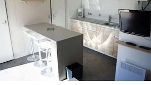 Una cocina compacta con barra, televisor integrado y un peque ño cubo de basura.
