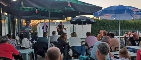 An outdoor seating area with tables and chairs, umbrellas, and a stage for live music.
