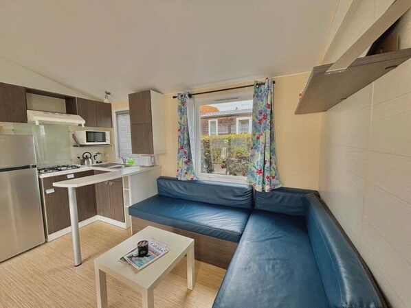 A compact living space with a kitchenette, a sofa, and a window with curtains. - ZEcamping 3* cottage BBQ clim 4 pers (Sigean)