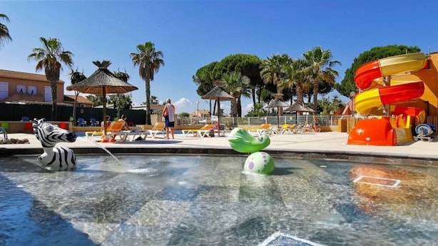 Een waterpark met een zebra-fontein, een glijbaan en een zwembadgedeelte met ligbedden.