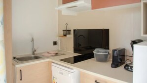 A compact kitchen with a sink, stove, and coffee maker. - ZEcamping 4 étoiles locatif TV LV BBQ 21m2 (Agde)