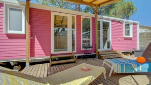 Una casa móvil rosa con una terraza de madera, una mesa pequeña y una piscina.