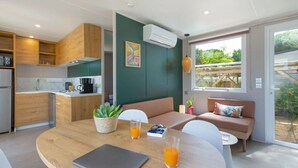 A modern kitchen with wooden cabinets, a dining table with two chairs, and a sofa with cushions. - ZEcamping 4* animé 1km plage piscine chauffée locatif TV LV BBQ 31m2 (Agde)