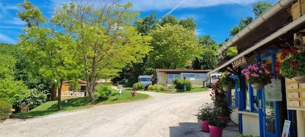 A rural road leading to a building with a blue facade and flower pots. - ZEcamping 3* piscine chalet TV clim 24m2 5 pers (Durfort)