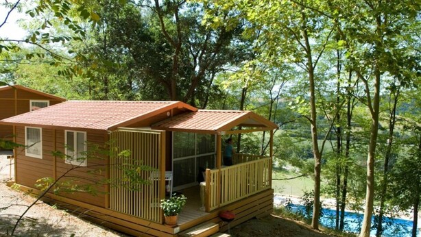 Une petite cabane dotée d’une terrasse, entourée d’arbres et bordée par un plan d’eau.