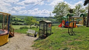 Une aire de jeux avec un trampoline, un toboggan et un petit abri.