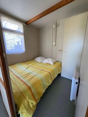 A small, single-bed room with a window, a wardrobe, and a built-in heater. - ZEcamping 3* piscine chalet TV clim 24m2 5 pers (Durfort)