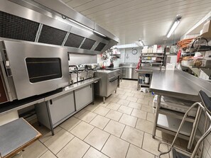 A commercial kitchen with stainless steel appliances, tiled flooring, and a clock on the wall. - ZEcamping 3* piscine chalet TV clim 24m2 5 pers (Durfort)