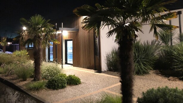 A modern building with a wooden facade and a gravel pathway leading to a glass door.