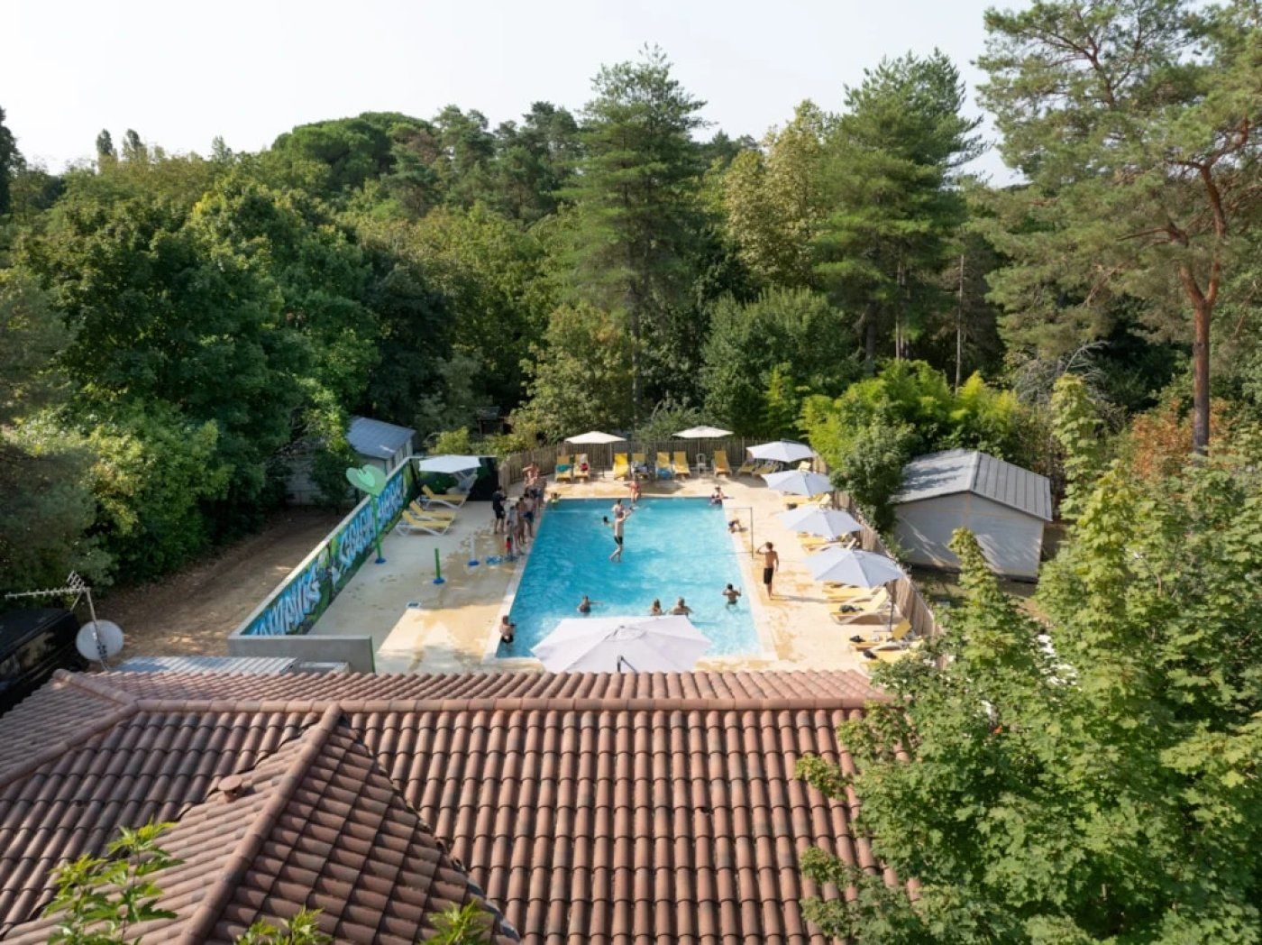 Ein Schwimmbecken, umgeben von Bäumen, mit Liegestühlen und Sonnenschirmen.