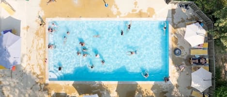 Vista aérea de una piscina con gente nadando, rodeada de tumbonas y sombrillas.