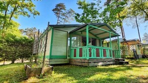 A small, green-roofed cabin with a porch, surrounded by trees and grass.