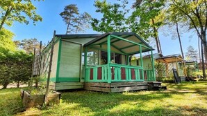 A small, green-roofed cabin with a porch, surrounded by trees and grass.