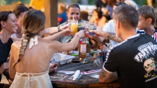 A group of people toasting at a wooden table with drinks and snacks.