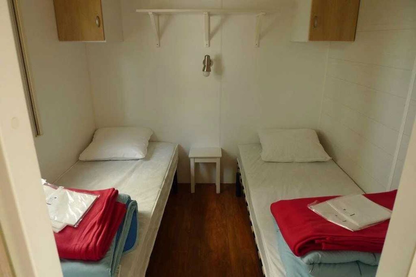 A small, compact room with two single beds, a small table, and a hanging light fixture.
