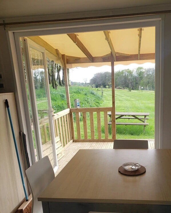 A room with a wooden table, a bench, and a view of a grassy area with a picnic table outside.