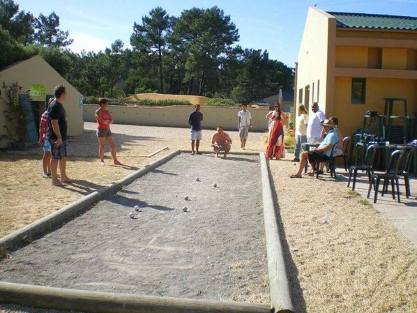 An outdoor area with a shuffleboard table, people standing around, and a building in the background.