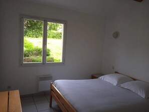 A bedroom with a single bed, a window with a view of greenery, and a small table.