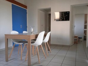 A dining area with a wooden table and white chairs, a blue door, and a framed picture on the wall.