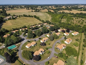 An aerial view of a residential area with houses arranged in a semi-circular pattern around a central road, surrounded by fields and trees.