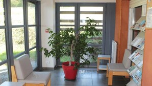 A reception area with a large window, a potted tree, and a seating area with chairs and a small table. - ZEcamping 2 étoiles piscine chauffée mobil-home TV 25m2 5 pers (Prailles-La Couarde)