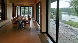A dining area with a long table and chairs, large windows with a view of a lake and greenery. - ZEcamping 2 étoiles piscine chauffée mobil-home TV 25m2 5 pers (Prailles-La Couarde)